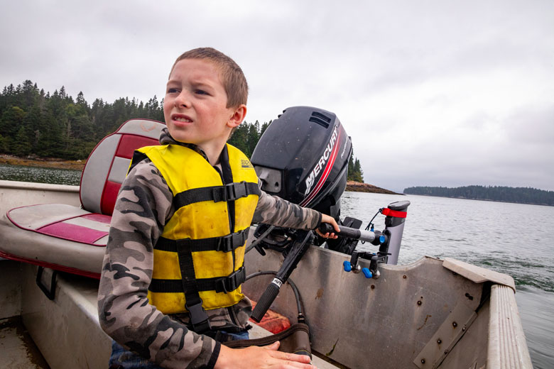 Luke Maker, 8, of Machiasport runs the family skiff through a cove earlier this summer using an electric outboard purchased through a grant from Island Institute, publisher of The Working Waterfront. Luke and is father, Ryan, fish for lobster. PHOTO: JACK SULLIVAN