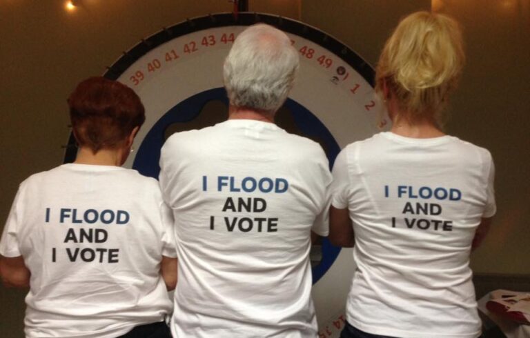 three people shot from behind with shirts that say "I flood and I vote"