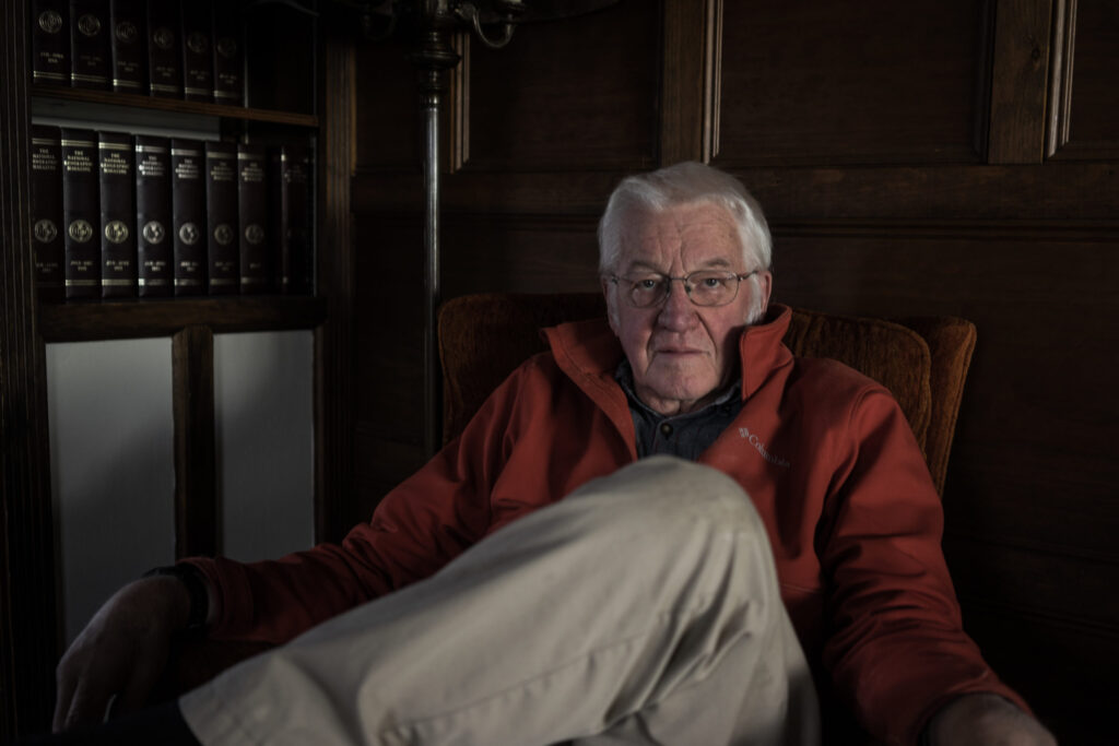 old man looking directly at camera sitting in dimly lit room