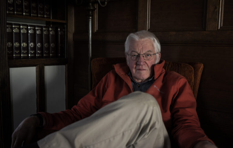 old man looking directly at camera sitting in dimly lit room