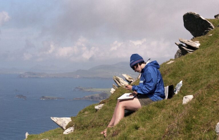 Woman sketching on a hill overlooking ocean