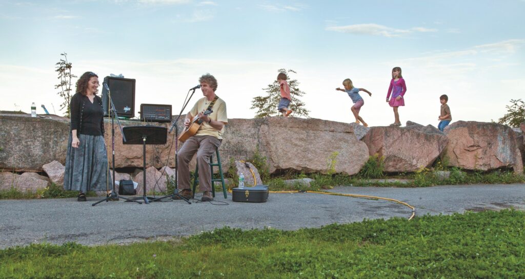 musicians performing on a sidewalk with young kids playing in the background