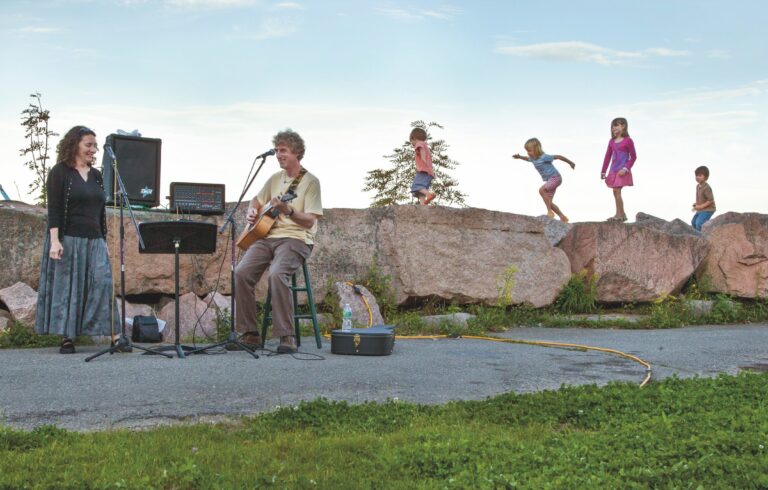 musicians performing on a sidewalk with young kids playing in the background