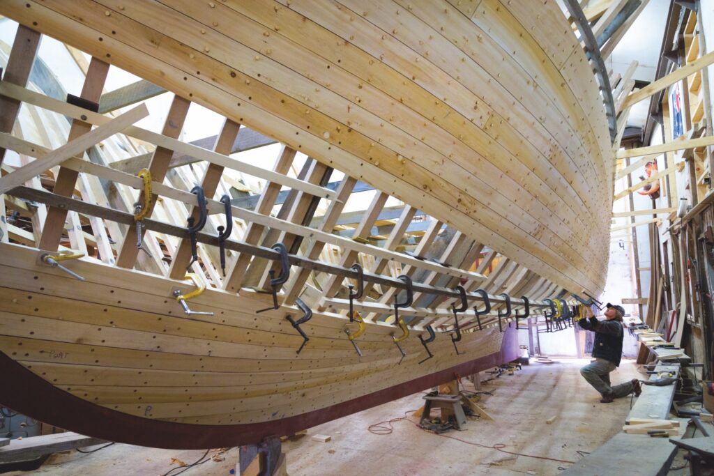 man working on building bottom of wooden boat