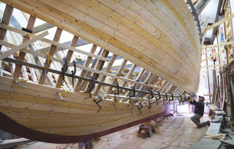 man working on building bottom of wooden boat