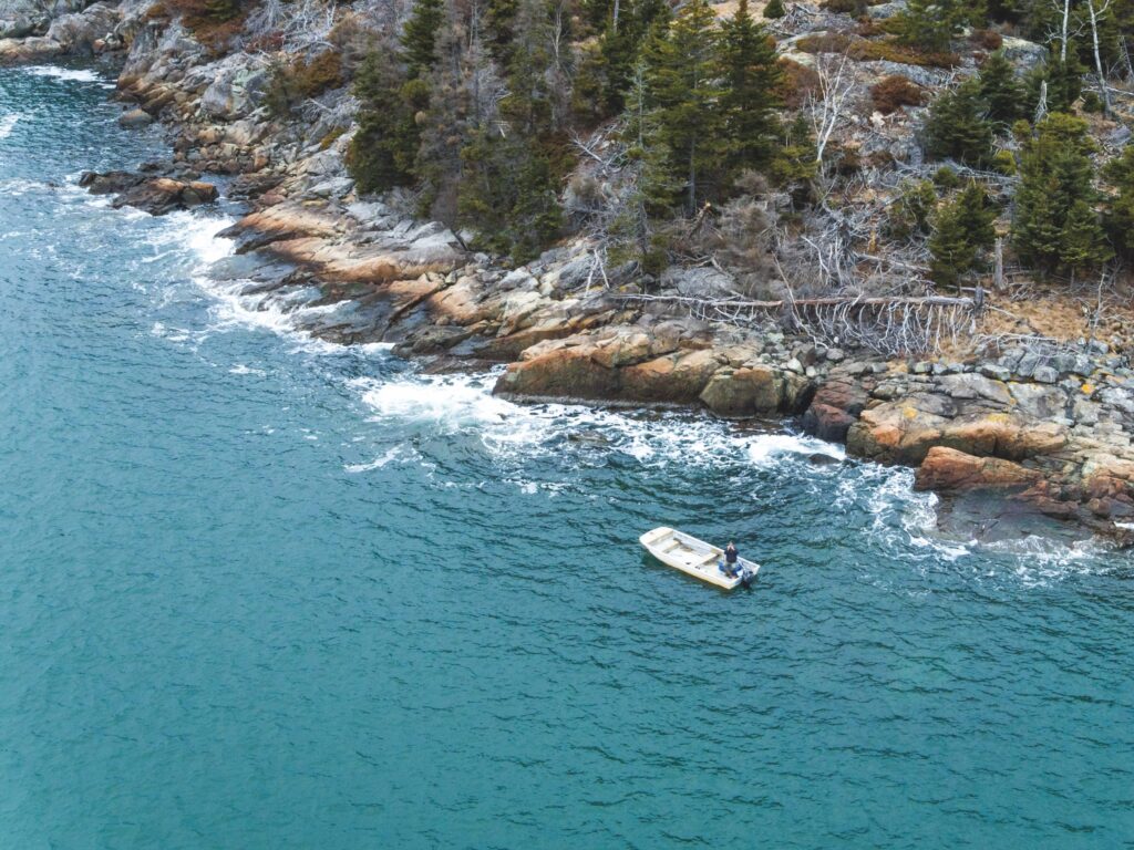 aerial shot of dinghy floating along rocky coastline