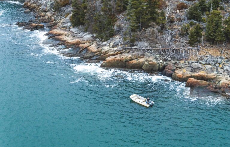 aerial shot of dinghy floating along rocky coastline