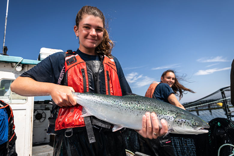 Megan Robinson, front, and Jessica Lindsay weigh fish at a Machias Bay salmon farm owned and operated by Cooke Inc. The New Brunswick-based company has been operating in Maine for 20 years. PHOTO: COURTESY COOKE INC.